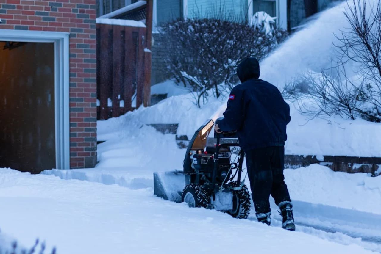 Un propriétaire opérant une souffleuse à deux étages sur une entrée enneigée canadienne au crépuscule — contexte concret pour les guides d’achat d’équipement snow.ca.