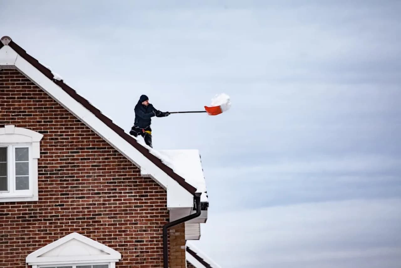 Roof snow removal crew clearing heavy snow load from a Canadian residential roof — fall-arrest certified.