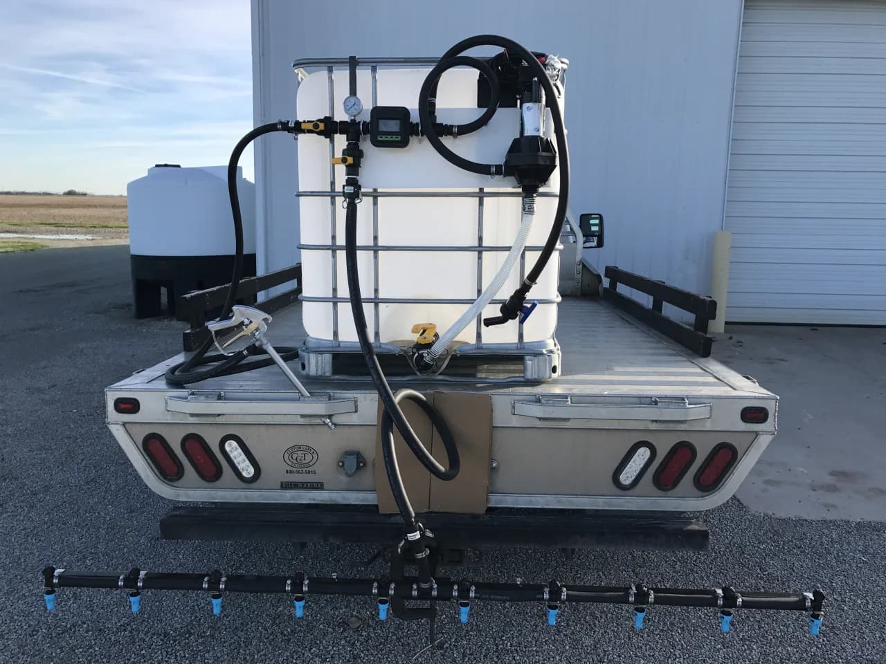 Truck-mounted IBC brine tote with electric pump, flow meter and rear spray boom — salt-brine applicator rig for snow.ca Canadian anti-icing pre-treatment routes ahead of forecast storms.