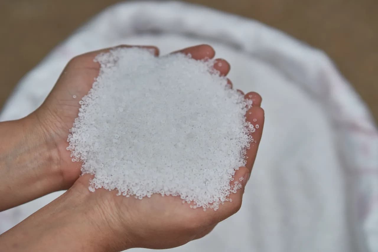 Open hands cupping a mound of white calcium-chloride de-icer pellets above the supply bag — strongest chloride de-icer effective to -32°C for Canadian deep-cold snow.ca commercial accounts.